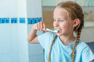 adorable niña se cepilla los dientes en el baño. foto