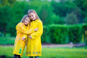 Cute toddler girls wearing waterproof coat playing outdoors by rainy and sunny day photo