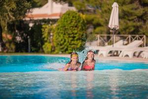 Adorable little girls playing in outdoor swimming pool on vacation photo