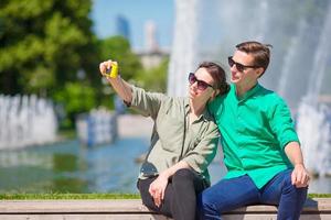 Couple taking a selfie background the fountain. Young man making photo of woman on the street laughing and having fun in summer.