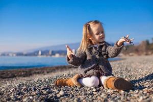 Adorable little girl on the beach in a cozy sweater and dress at warm winter day photo