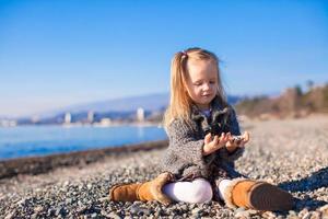 Adorable little girl on the beach in a cozy sweater and dress at warm winter day photo