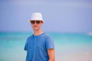 Young man enjoying the music on white sandy beach. Happy tourist relaxing on summer tropical vacation. photo