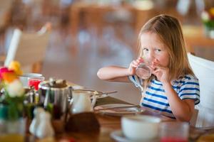 Little kid having breakfast at outdoor cafe. Adorable girl drinking fresh watermelon juice enjoying breakfast. photo