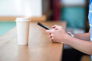 Closeup of male hands holding cellphone and glass of coffee in cafe. Man using mobile smartphone. Boy touching a screen of his smarthone. photo