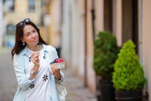 Woman with berries on the old street in the city. Blueberries, raspberries, strawberries, cherries and blackberries in small basket. Gardening, agriculture, harvest and forest concept. photo