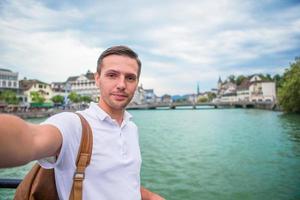 joven tomando selfie antecedentes famosa iglesia fraumunster y río limmat, suiza. foto