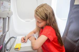 Adorable little girl traveling by an airplane. Kid drawing picture with colorful pencils sitting near window photo