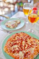 Pizza with mozzarella cheese, olive, fresh tomato and pesto sauce. Served at restaurant table with two beers photo