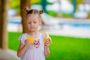 Adorable little girl with juice and banana at outdoor cafe. Fresh food and fruits in exotic country photo