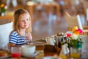 Little kid having breakfast at outdoor cafe. Adorable girl drinking fresh watermelon juice enjoying breakfast. photo