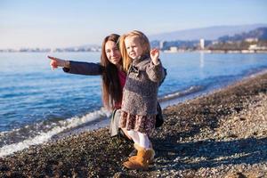 Little girl with mom having fun on the beach in a winter day photo