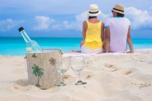 Bottle of white wine and two glasses background happy couple on sandy beach photo