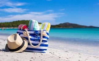 Blue bag, straw hat, flip flops and towel on white tropical beach photo