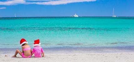 Little adorable girls in Santa hats during their beach tropical vacation photo