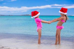 Little cute girls in Christmas hats having fun on exotic beach photo