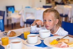 Adorable little girl having breakfast at restaurant photo