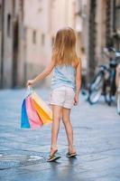 retrato de una adorable niña caminando con bolsas de compras al aire libre en una ciudad europea. foto