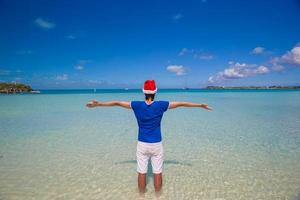 Back view of young man in santa hat on tropical beach photo