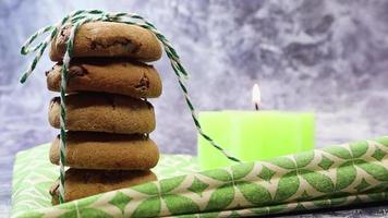 uma pilha de biscoitos de chocolate americanos amarrados com barbante em um guardanapo verde com uma vela acesa. tradicional massa crocante redonda com gotas de chocolate. padaria. deliciosa sobremesa, bolos. video
