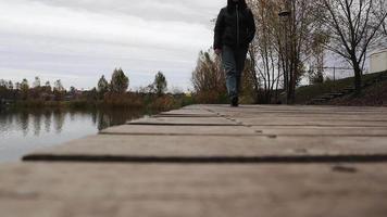 A woman walking in boots, jeans and a jacket on a wooden bridge over a lake in autumn weather, a cheerful happy journey without worries. Relaxation, enjoying life in nature, low viewing angle.