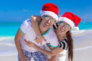 Retrato de joven pareja con sombreros de santa disfrutar de vacaciones en la playa foto