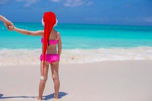 Back view of cute girl in red hat santa claus on the beach photo