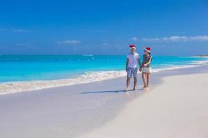 joven pareja feliz con sombreros rojos de santa en la playa de arena tropical foto