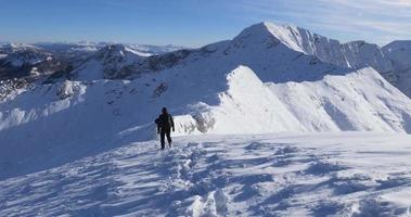 Solo-Wanderer auf dem Weg zum Berggipfel mit herausforderndem Bergrücken dazwischen. weite winterliche Berglandschaft voller Schnee. Wandern im Winter. Reise- und Freigeistgefühl. video