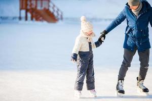 Young father and adorable little girl have fun on skating rink outdoors photo