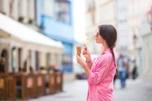 Young female model eating ice cream cone outdoors. Summer concept - woman with sweet ice-cream at hot day photo