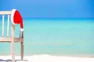 Santa Claus Hat on chair near tropical beach with turquoise sea water and white sand. Christmas vacation concept photo