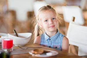 Little smiling girl having lunch in outdoor cafe photo