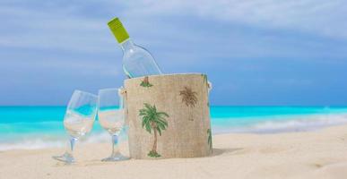 botella de vino blanco y dos copas en la exótica playa de arena foto