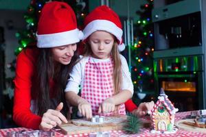 Happy mom and little girl in Santa hat baking Christmas gingerbread cookies together photo