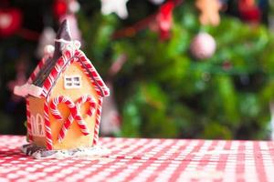 Gingerbread house decorated by sweet candies on a background of bright Christmas tree with garland photo