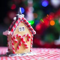 casa de hadas de pan de jengibre de primer plano decorada con dulces coloridos sobre un fondo de árbol de navidad brillante con guirnalda foto