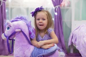 Cute little funny girl playing with a toy horse at home photo