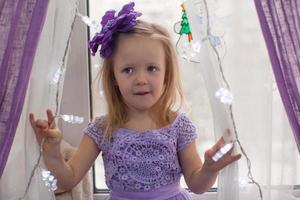 Little adorable girl in beautiful dress among garlands at home photo