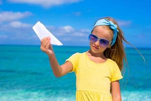 Happy little girl with paper airplane during beach vacation photo