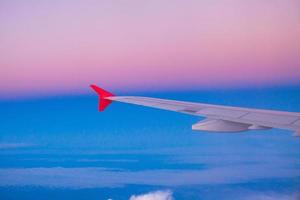 Wing of an airplane flying above the clouds in colorful sky photo