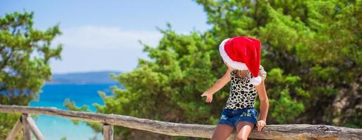 Adorable little girl in christmas hat during summer beach vacation photo