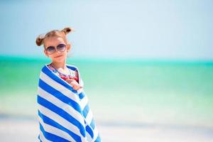 adorable niña envuelta en una toalla después de nadar en una playa tropical foto