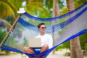 joven con laptop en hamaca en vacaciones tropicales foto