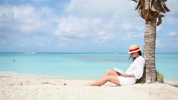 ung kvinna läsning bok under tropisk vit strand video