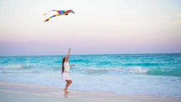 Adorable little girl with flying kite on tropical beach. Kid play on ocean shore with beautiful sunset video