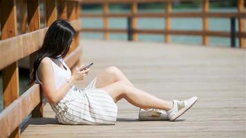 linda mulher está lendo mensagem de texto no celular enquanto está sentado no parque. video