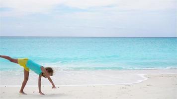 niña activa en la playa divirtiéndose mucho. niño deportivo hace la rueda en la orilla del mar en cámara lenta video