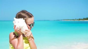 Portrait of little cute girl listening a big seashell on the beach. Slow motion video