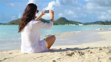 ung kvinna liggande på vit sand och talande förbi henne telefon video